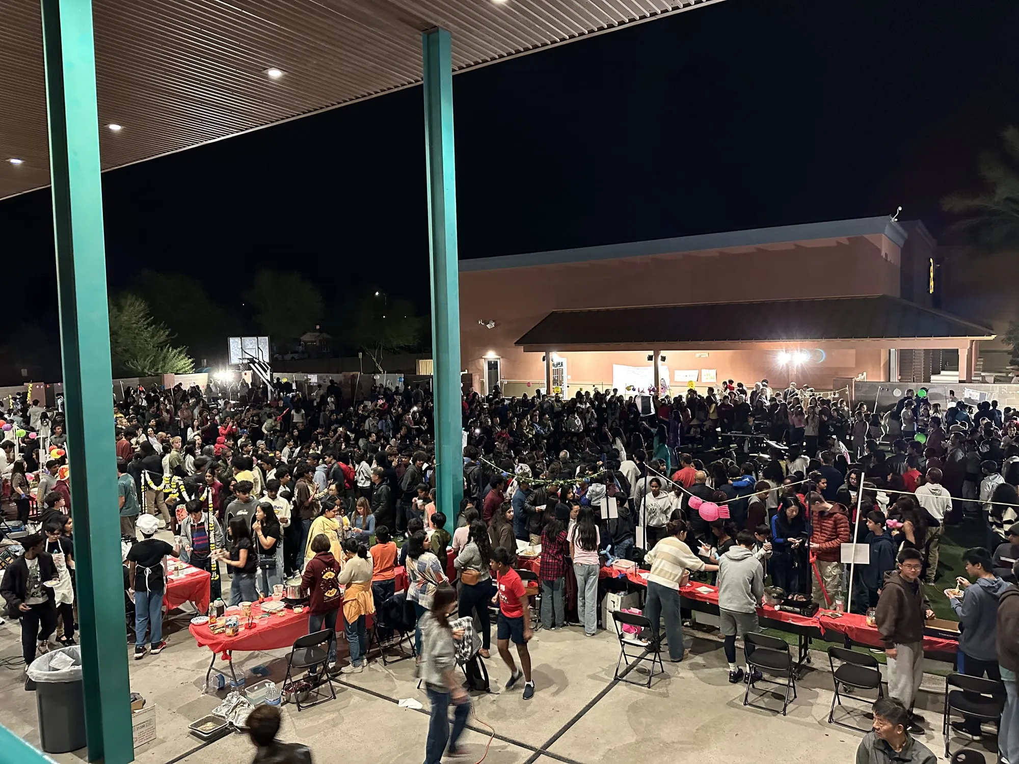 An overhead view of a packed courtyard at night, lined with red booth tables