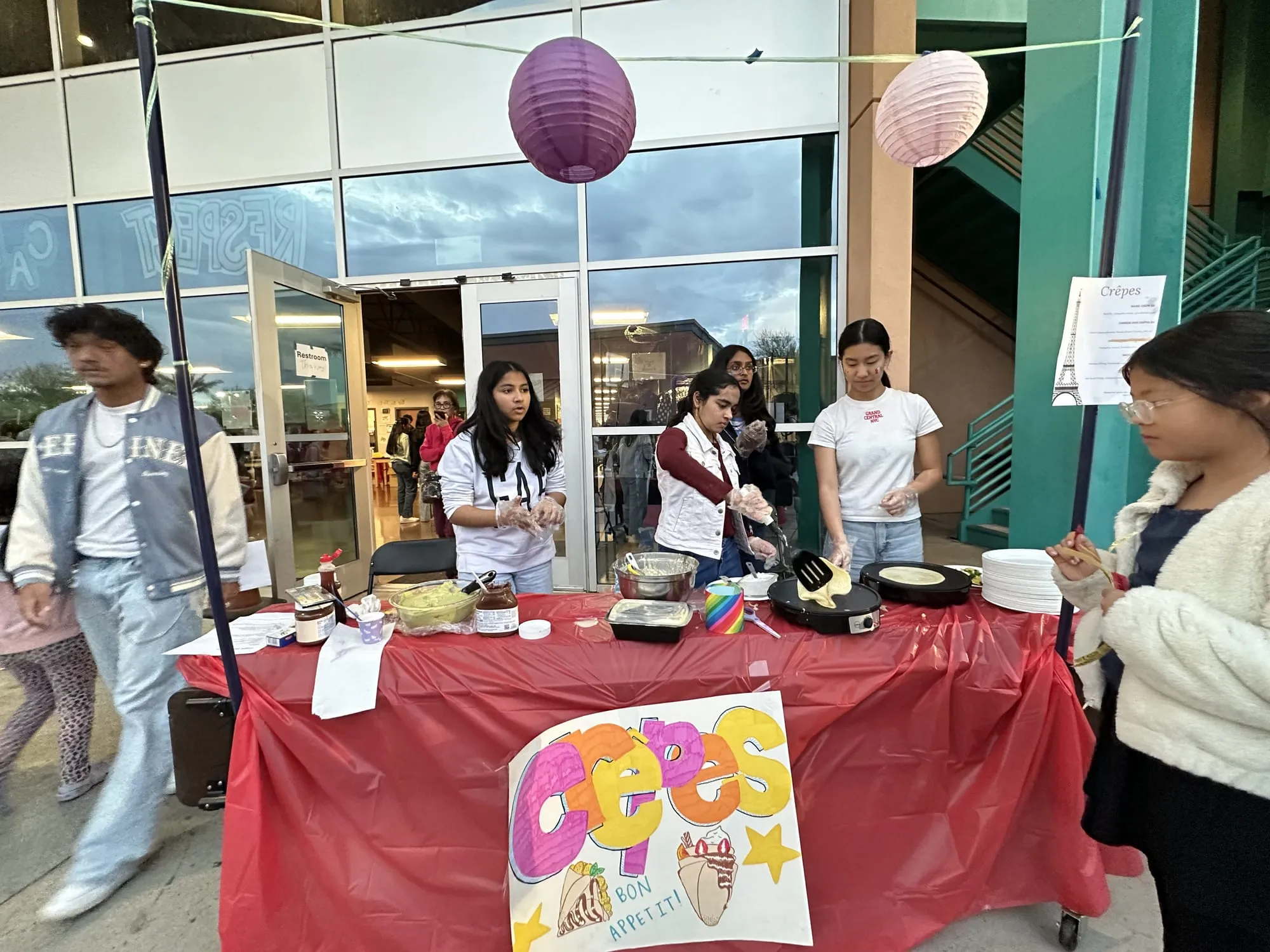 Students cook crepes at a booth with a colorful hand-drawn sign