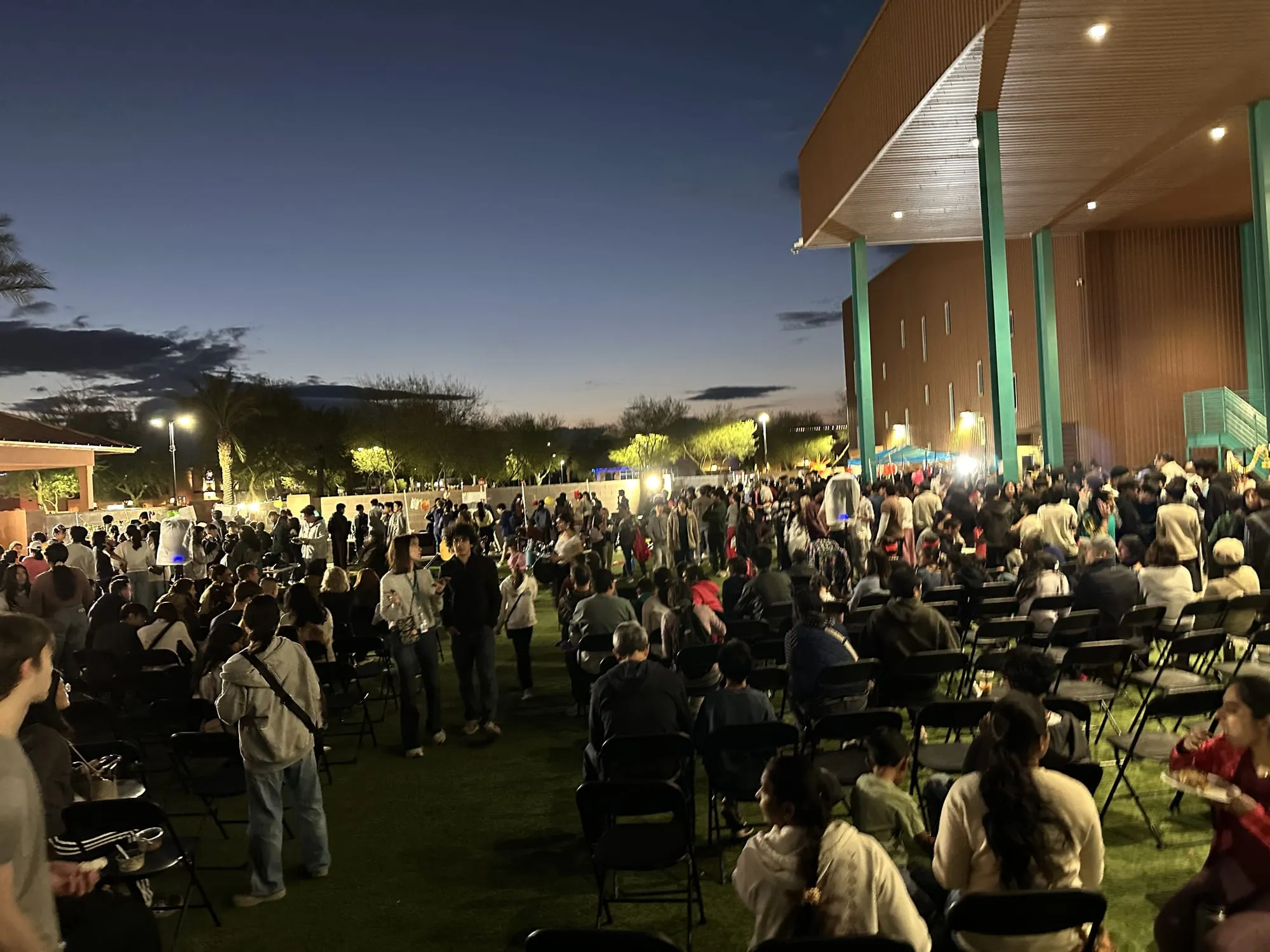 A large crowd fills the lawn at dusk under a deep blue sky