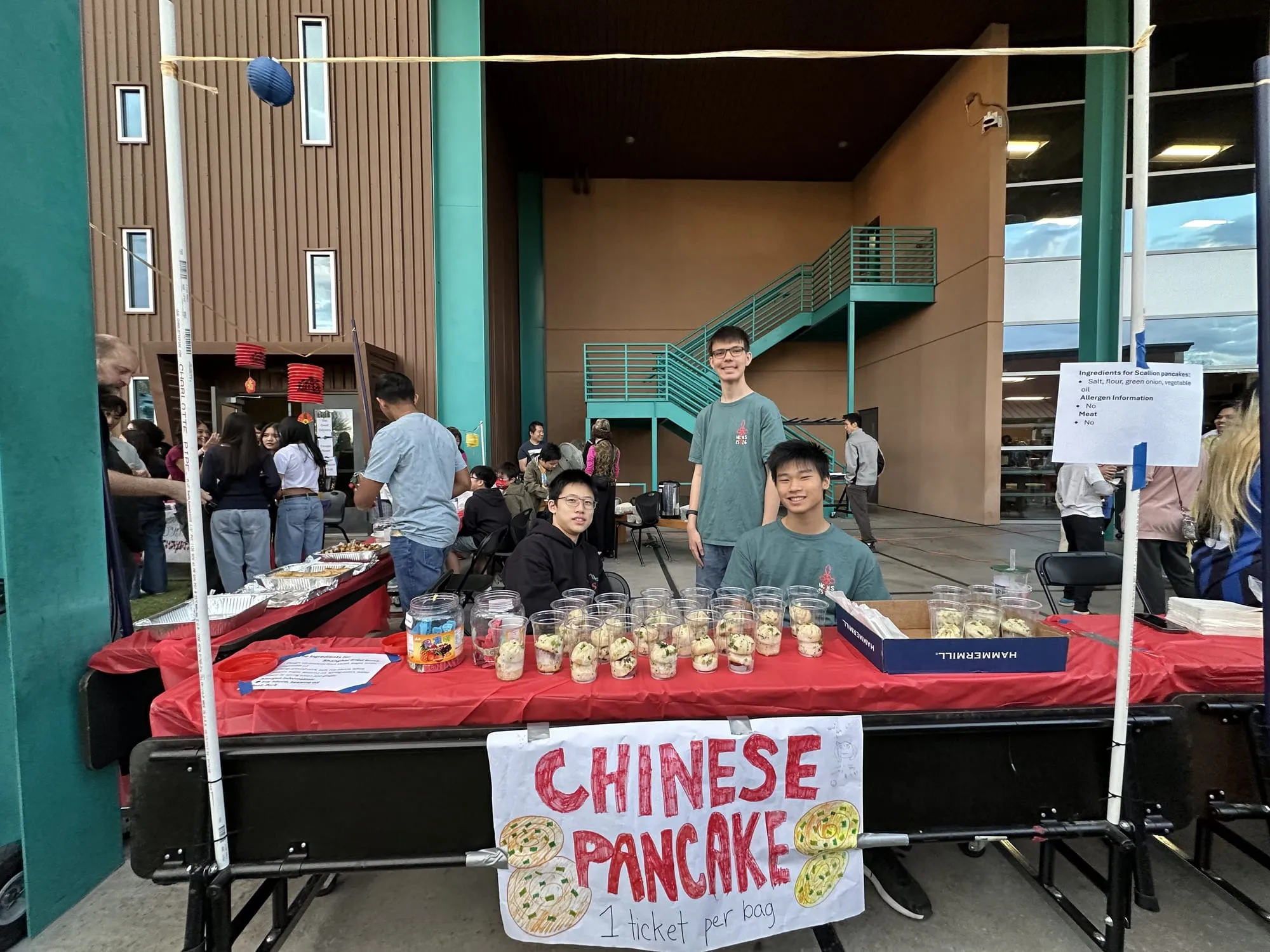 Students at a Chinese pancake booth with cups of pancake bites on a red table
