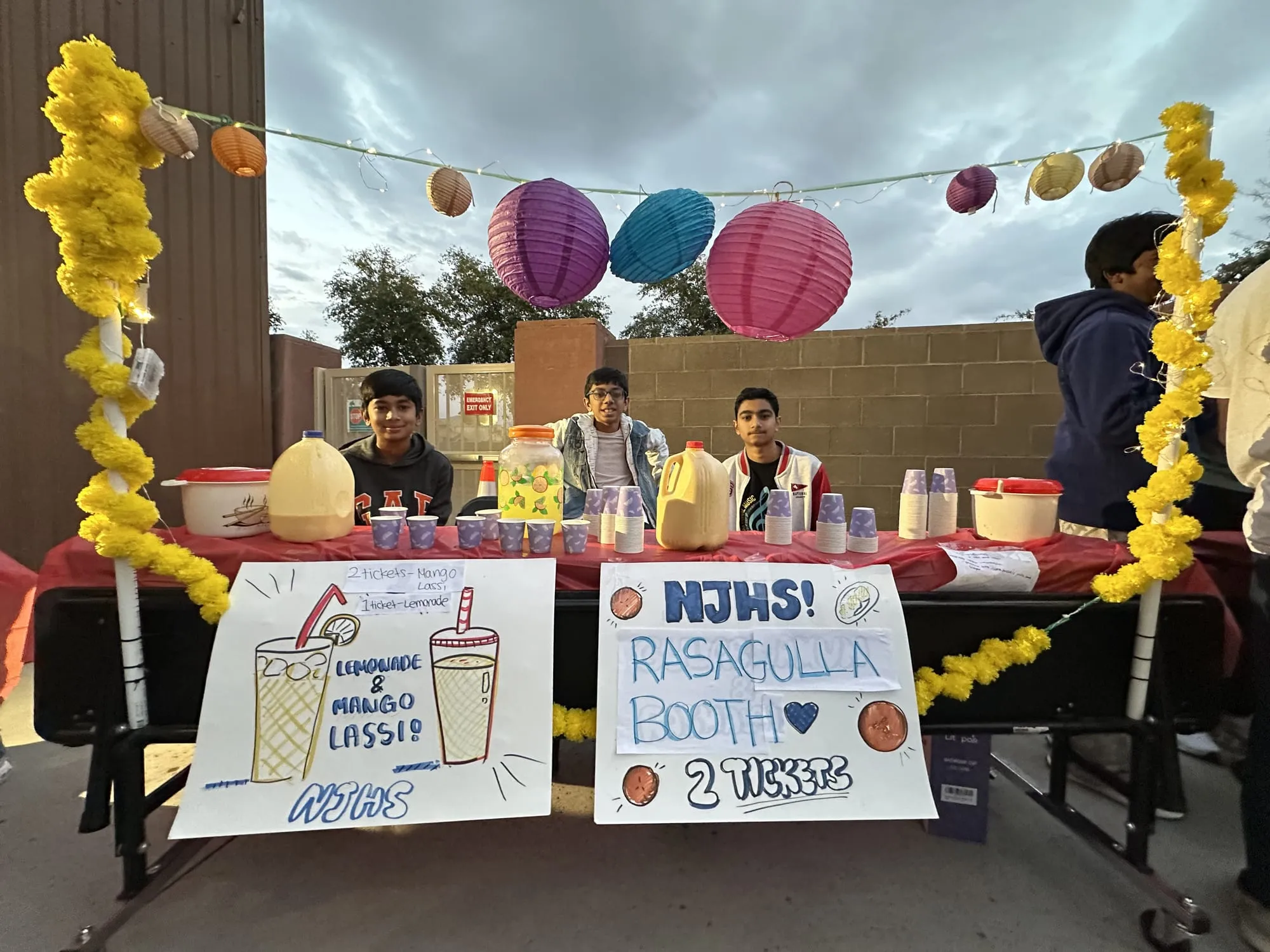 A booth selling lemonade, mango lassi and rasagulla under paper lanterns and marigolds