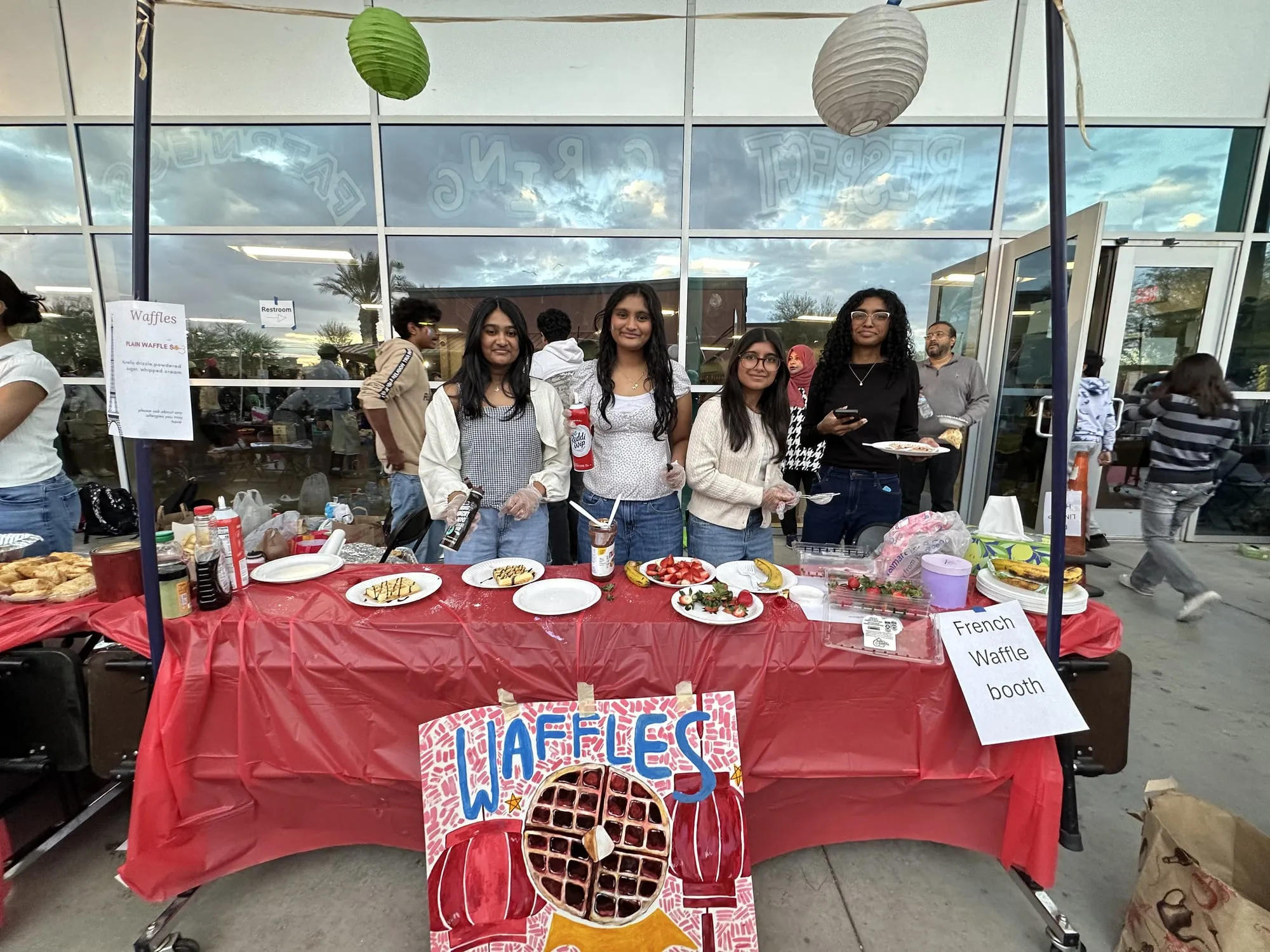 Students behind a waffle booth decorated with a lantern-themed sign